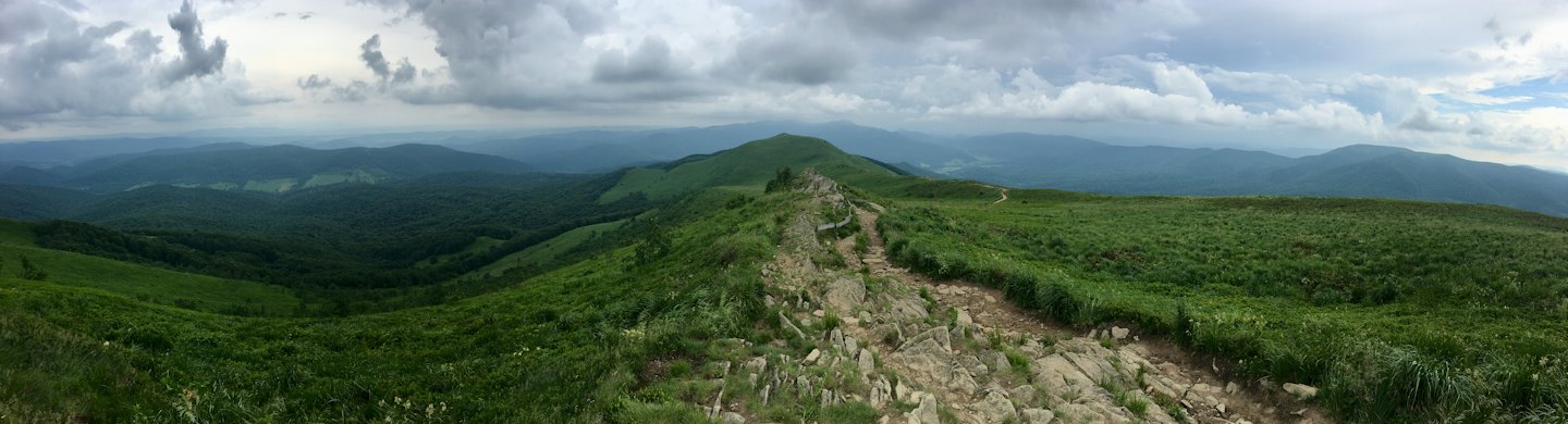 A winding hiking trail crosses a green mountain ridge.